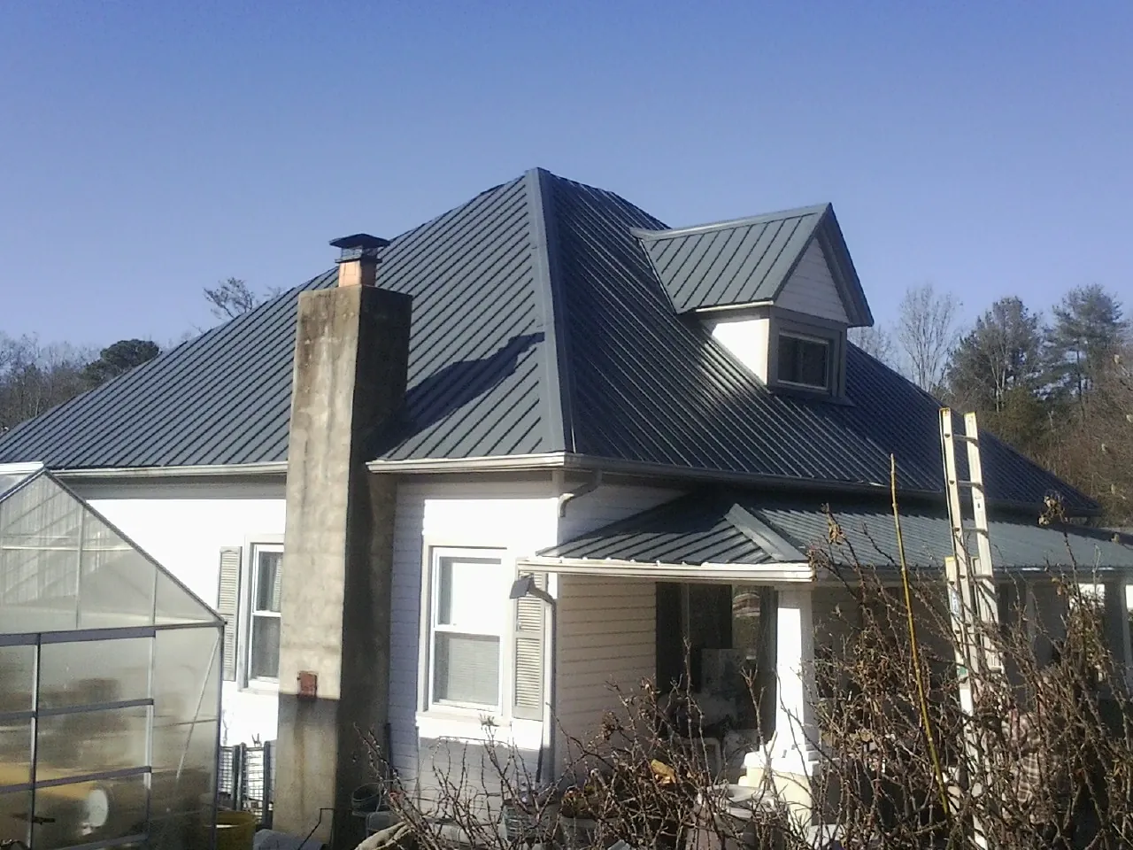 Dark blue standing seam metal roof on a white farmhouse with dormer — Slate & Tile Roof Repair by Roofing Brothers in Olin