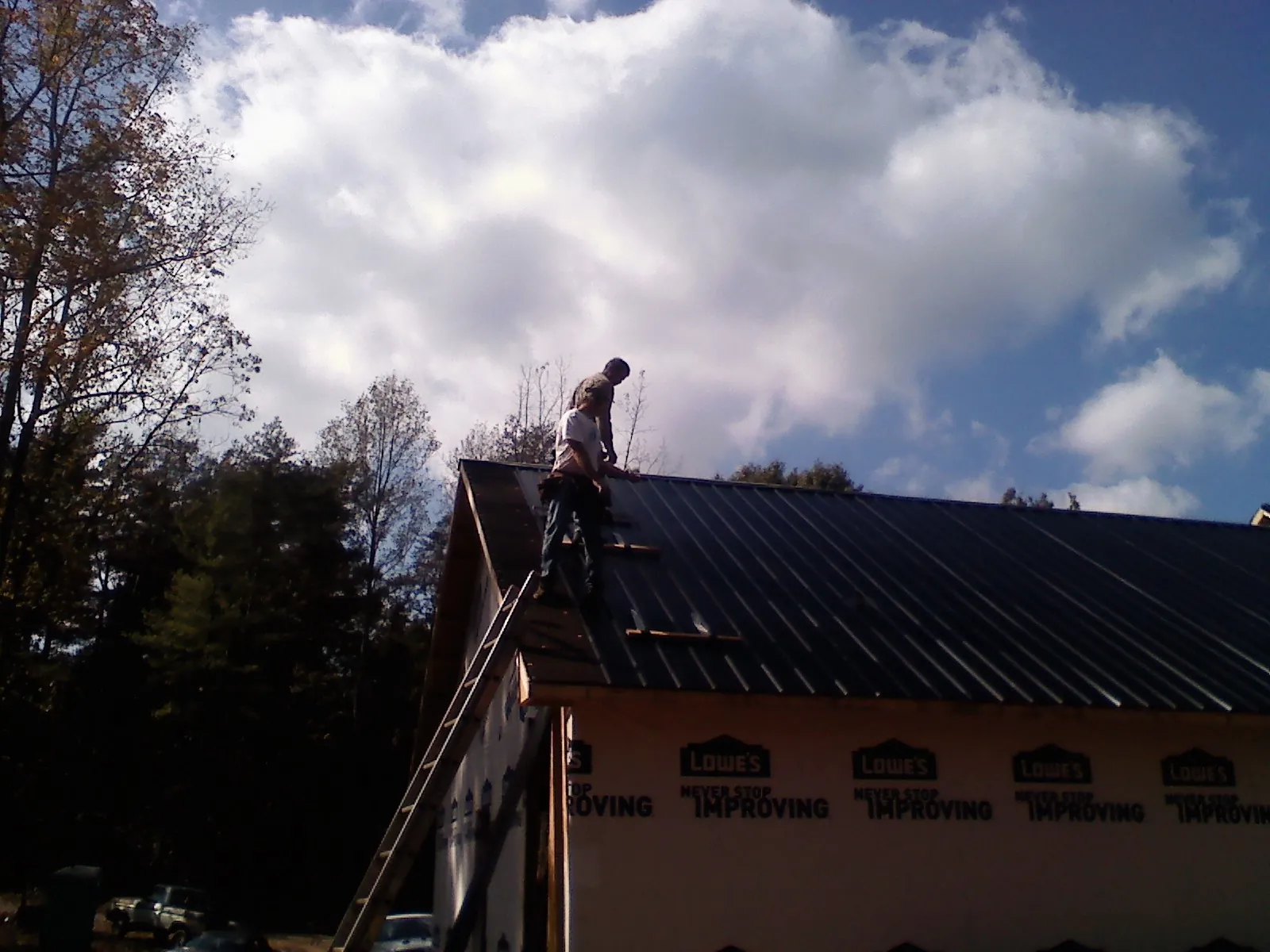 Roofer fastening dark metal panels high against a cloudy sky, from a Roof Inspection job in Olin