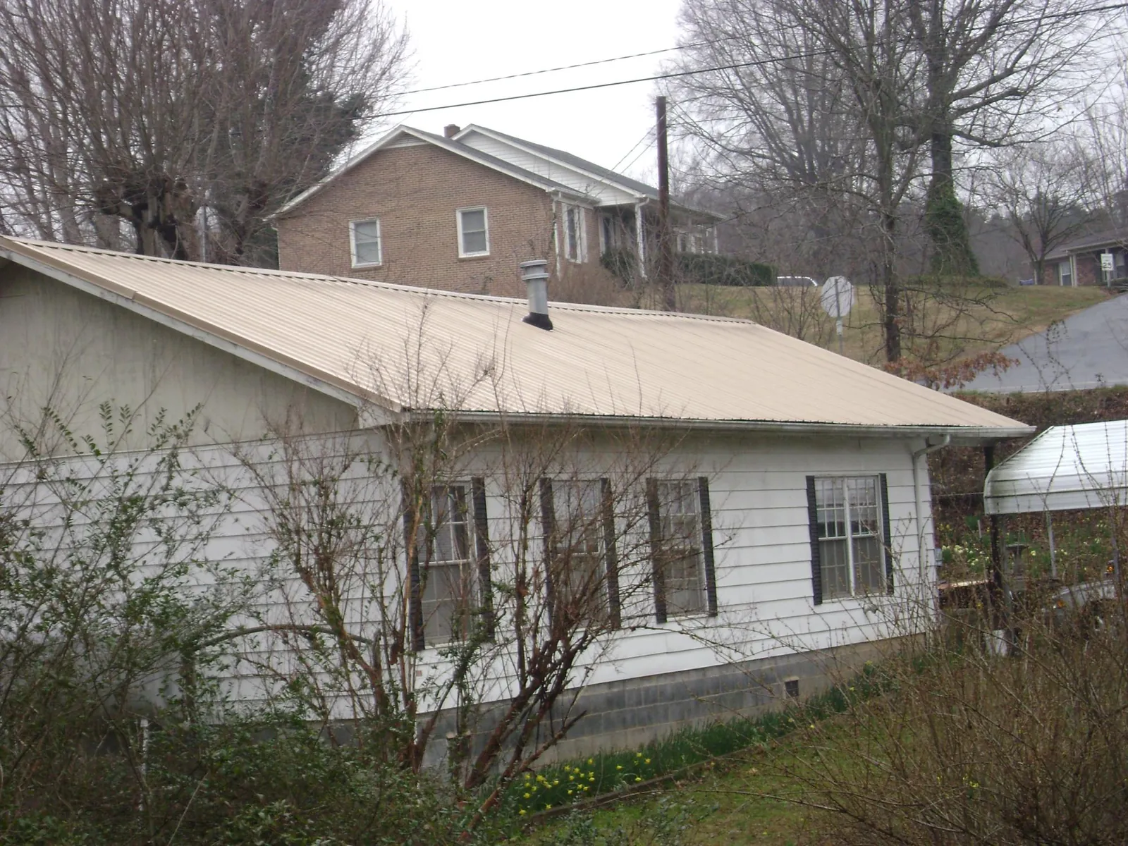 Tan metal roof on a white sided house set into a hillside — Commercial Roofing by Roofing Brothers in Olin