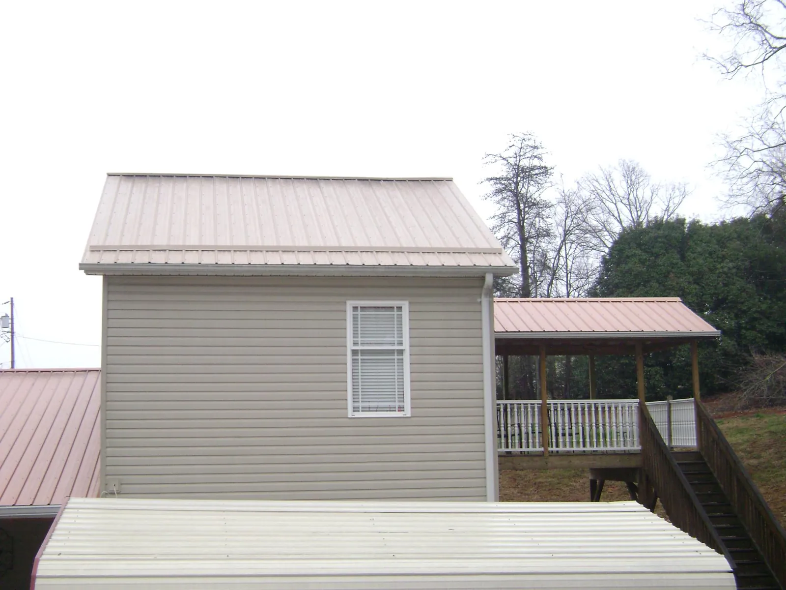 Tan metal roofs on a two story addition and attached porch, from a Roof Replacement job in Olin