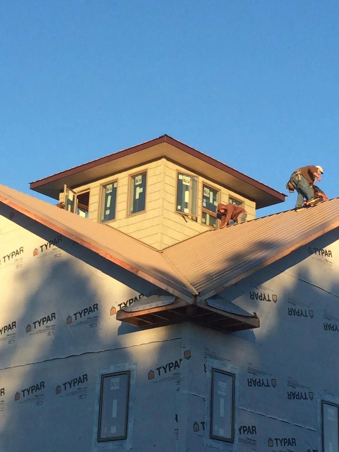 Roofers working around a rooftop cupola on a new metal roof at sunset — Roof Waterproofing in Olin by Roofing Brothers